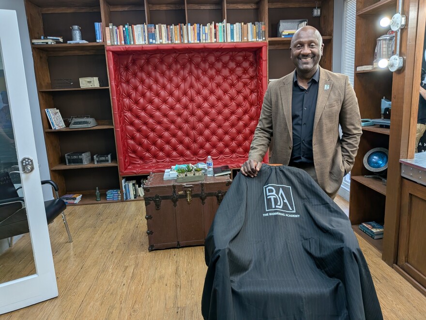 Gale Nelson stands behind a draped barber chair in a barber shop studio.