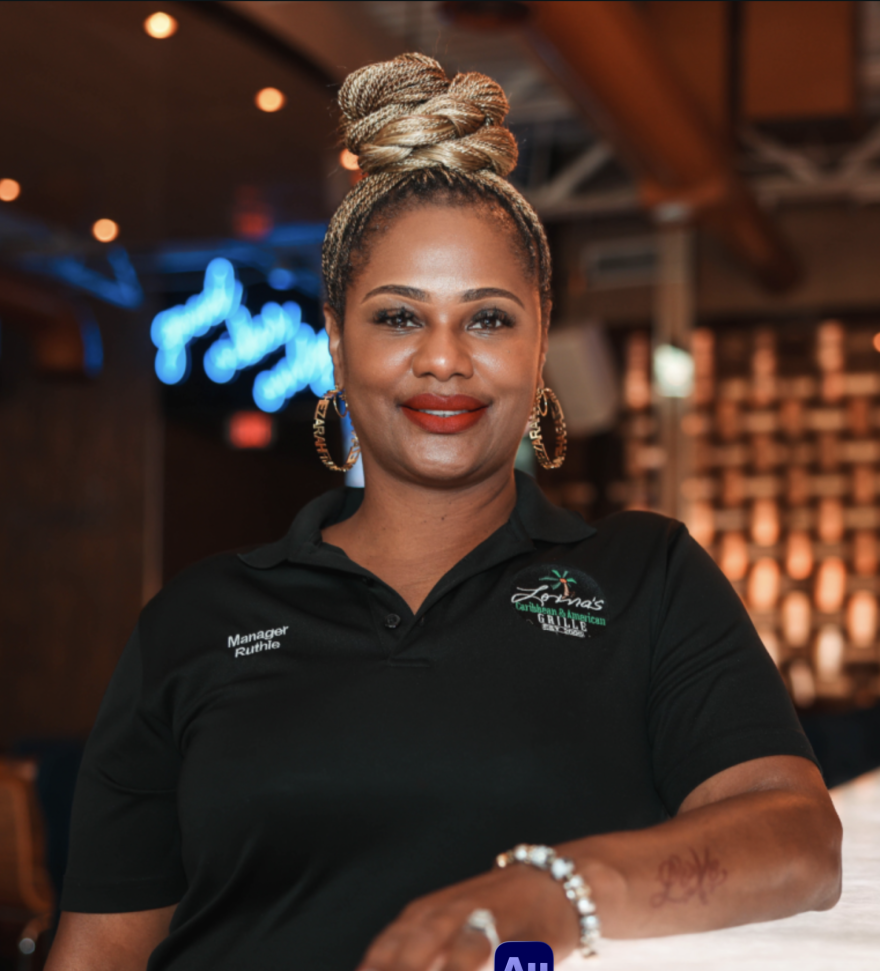 Ruthie Bodie stands with her arm across the bar in a Caribbean-themed restaurant.