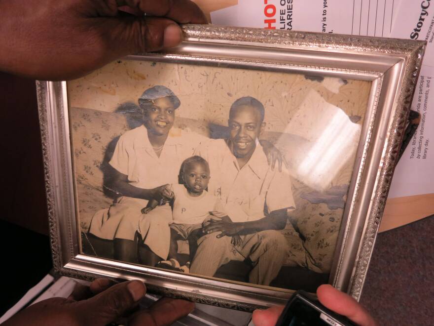 Man holds black and white framed photograph of a young boy with two parents