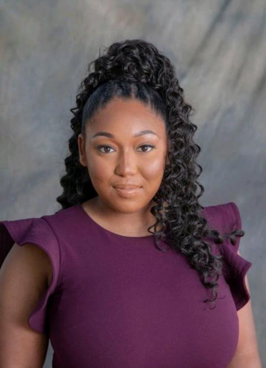 A young Black woman dressed in a burgundy top with her dark hair cascading over her shoulders looks toward the camera.