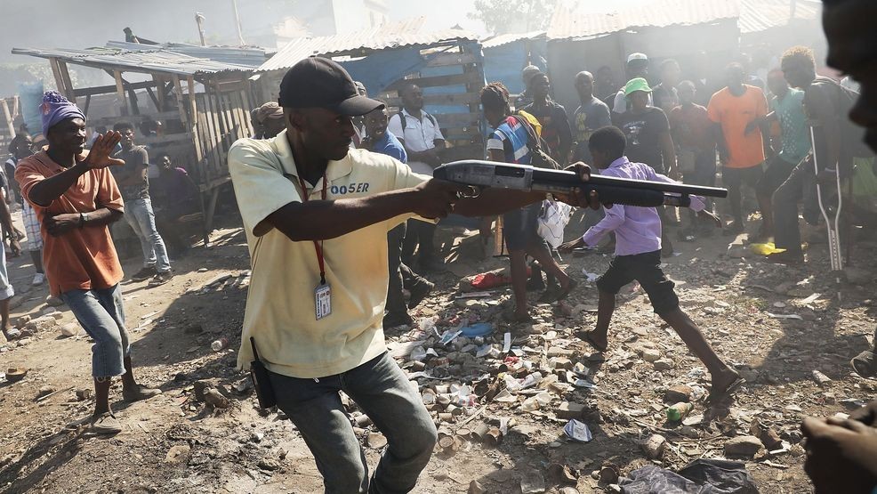 PORT-AU-PRINCE, HAITI - FEBRUARY 13: A member of a security force chases crowds with a gun following a fire at Port-au-Prince's historic Iron Market on February 13, 2018 in Port-au-Prince, Haiti. Hundreds of locals vendors lost all of their merchandise in the early morning blaze which is still under investigation. Haiti, the poorest country in the Western Hemisphere, is still reeling from President Donald Trump's comments about the Caribbean nation and his decision to revoke Temporary Protected Status (TPS) for Haitians living in America following the 2010 earthquake that claimed over 300,000 lives. Haiti is currently preparing for the start of Carnival on Sunday. (Photo by Spencer Platt/Getty Images)