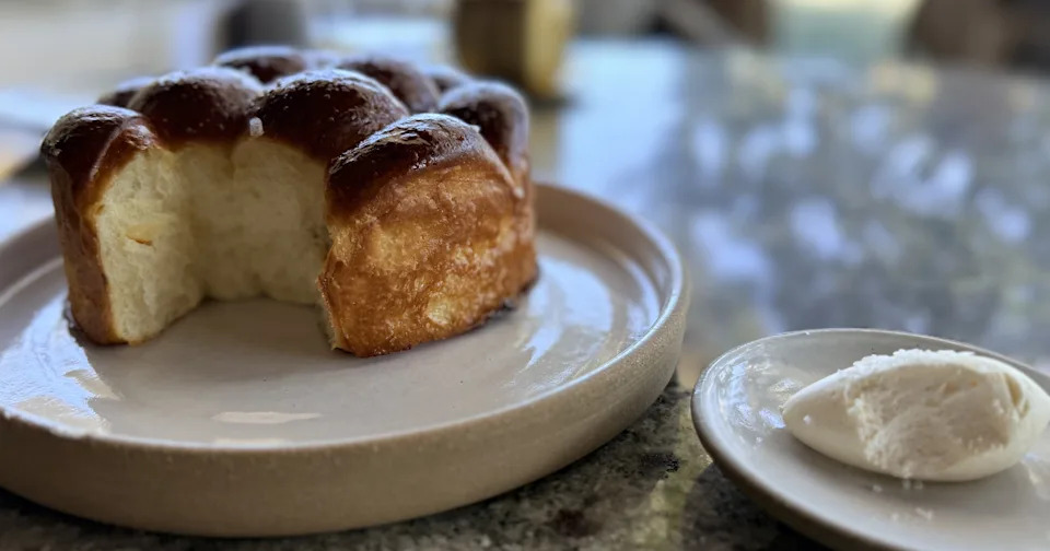Freshly baked, layered brioche pull-apart bread served in a small pan with a side of wildflower honey butter.