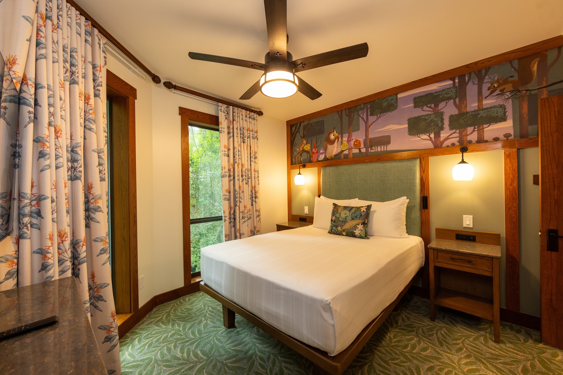 Queen Bed in a Forest themed Hotel Room with a Mural Above the Headboard Two Nightstands and Warm Lighting from Wall Lamps