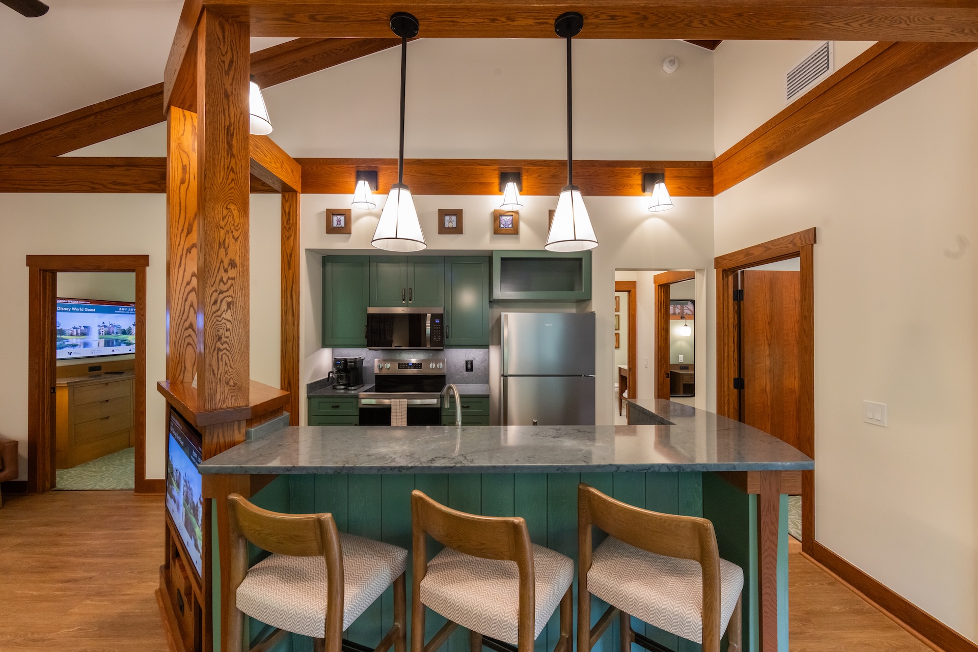 Kitchen with Teal green Cabinets Stainless Steel Appliances and a Marble Island Under Three Pendant Lights in a Wood beamed Room Capable of Hosting Bar Seating with Four Chairs Nearby