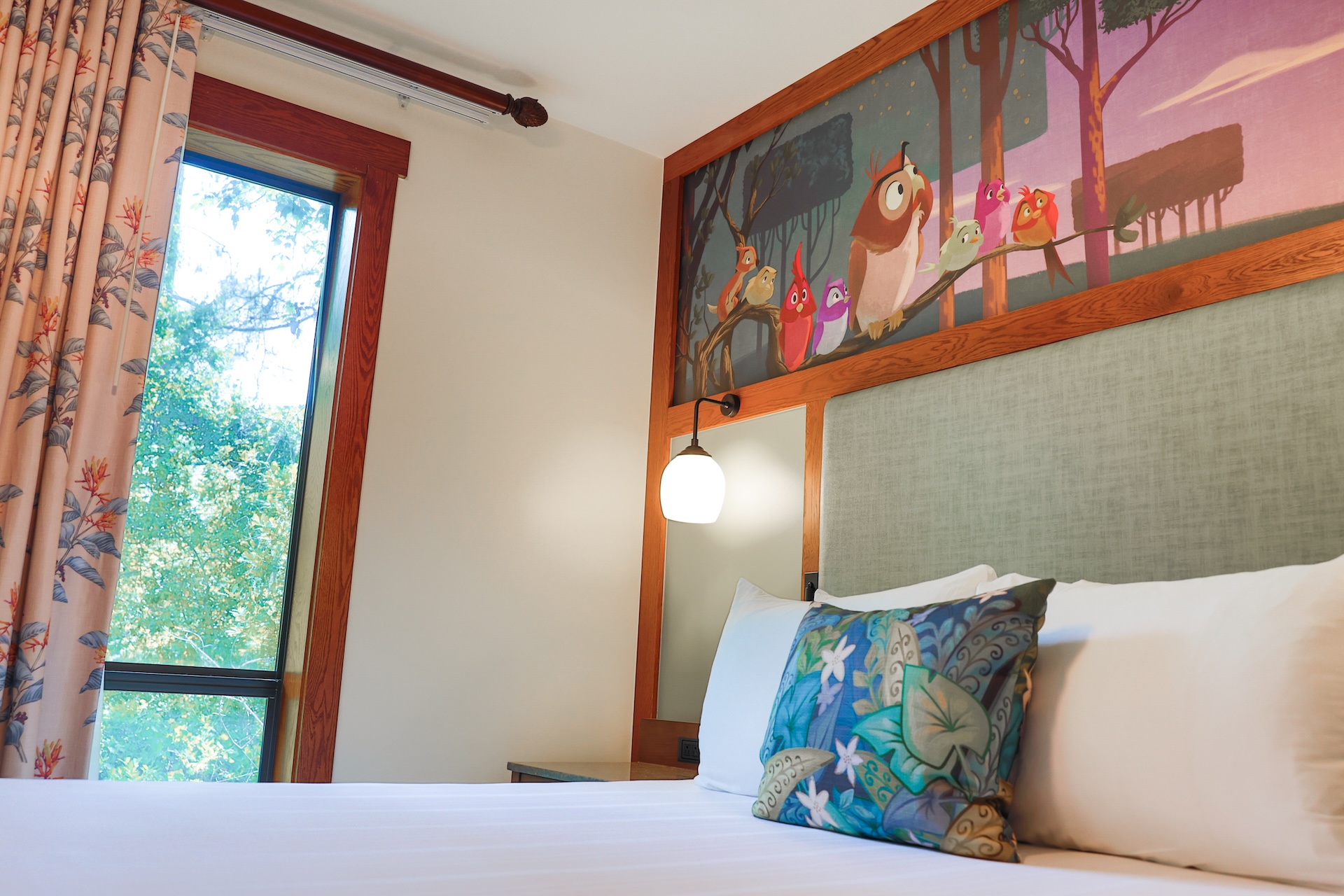 Hotel Bedroom with a Wooden Headboard White Bedding and Colorful Patterned Pillows in Front of an Owl Mural on the Wall
