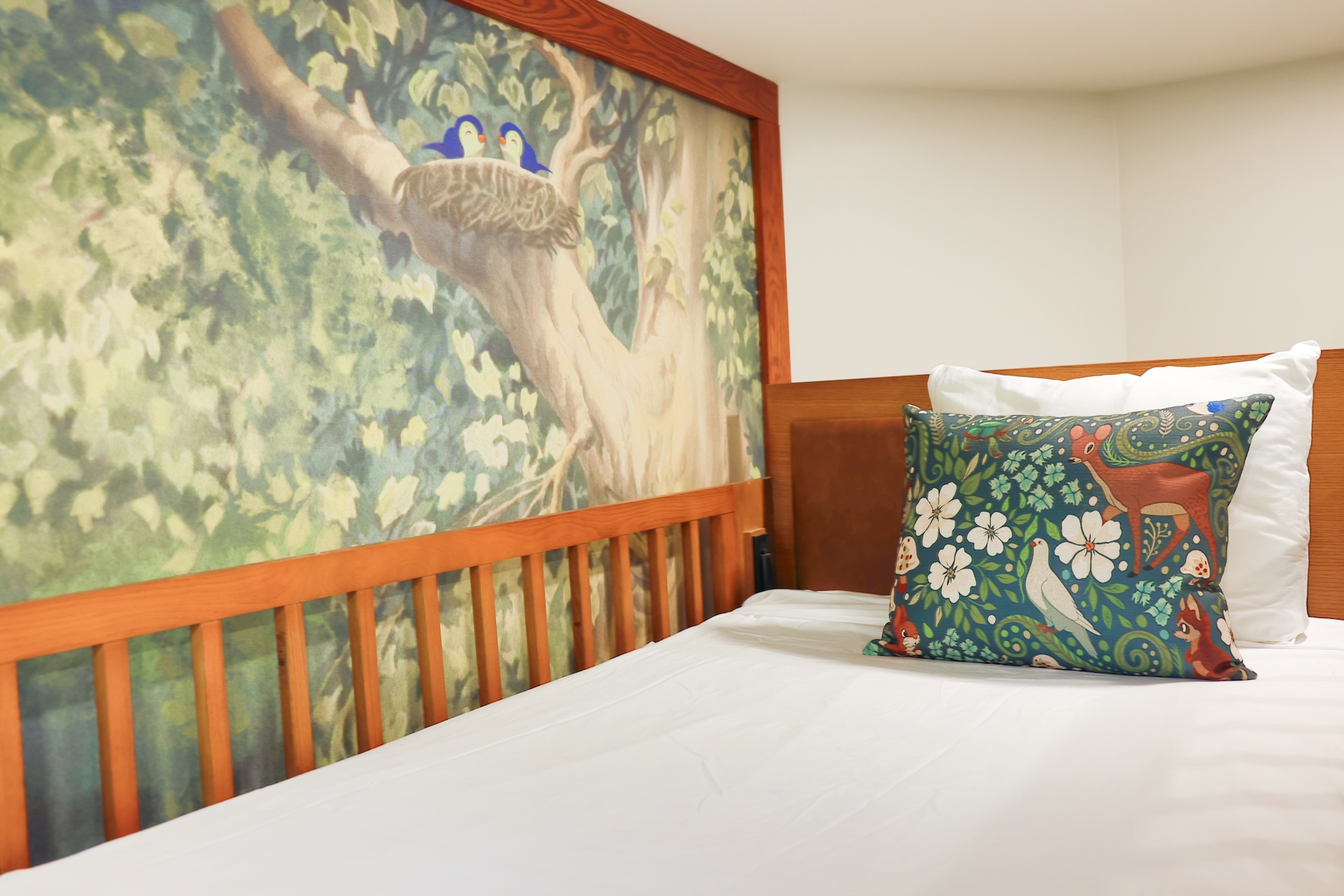 Bedroom with a Mural of Two Blue Birds Perched in a Tree Above a Wooden Headboard White Sheets and Decorative Pillows