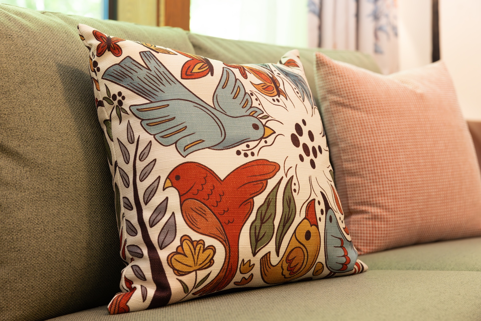 Colorful Decorative Throw Pillow with Birds and Flowers on a Beige Sofa Foreground Focus