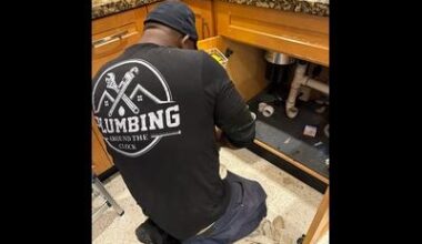 A skilled technician from Plumbing Around the Clock is pictured performing a precise under-sink repair in a residential kitchen. Wearing the company