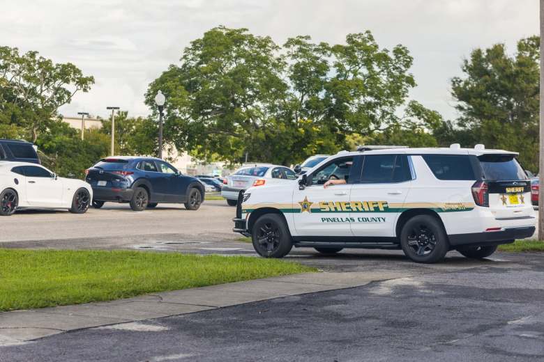 A white and green Pinellas County Sheriff's Office Chevrolet Tahoe patrol vehicle parked on a paved lot next to a roadway, with other cars and trees visible in the background under a cloudy sky.