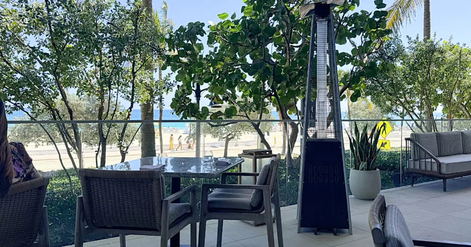 Outdoor terrace seating at MAASS restaurant in Fort Lauderdale with views of green trees, A1A, and the Atlantic Ocean.