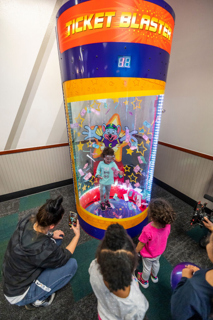 Young girl excitedly catching prize tickets inside the Ticket Blaster at Chuck E. Cheese.
