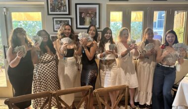 photo of eight women posing together in a row holding up dozens of $100-dollar bills