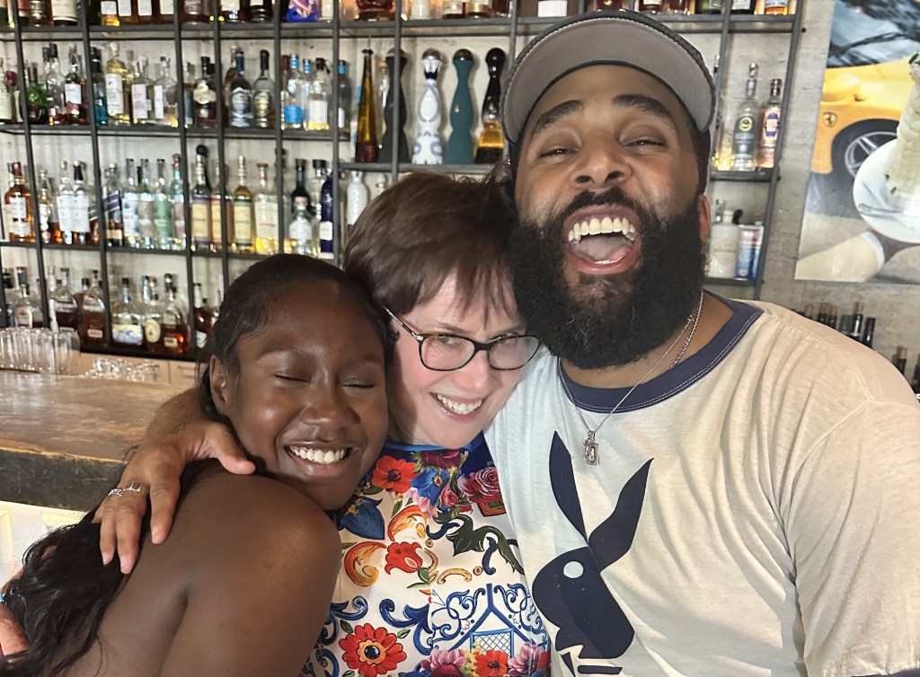 photo of two women and a man smiling and posing together in front of a bar