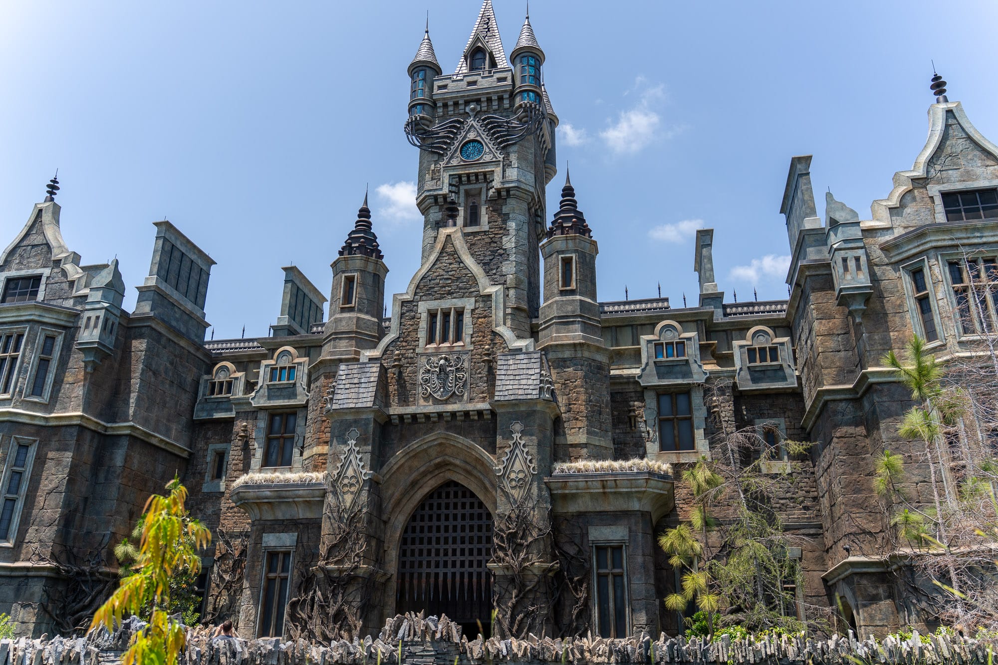 A large, dark, gothic-style castle with epic spires and detailed stonework rises under a clear sky.