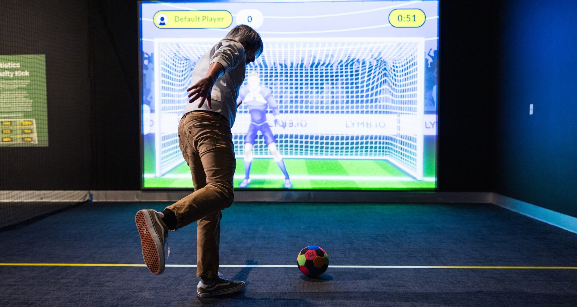 photo of a person kicking a soccer ball in front of an interactive screen showing an animated goalie in front of a soccer net
