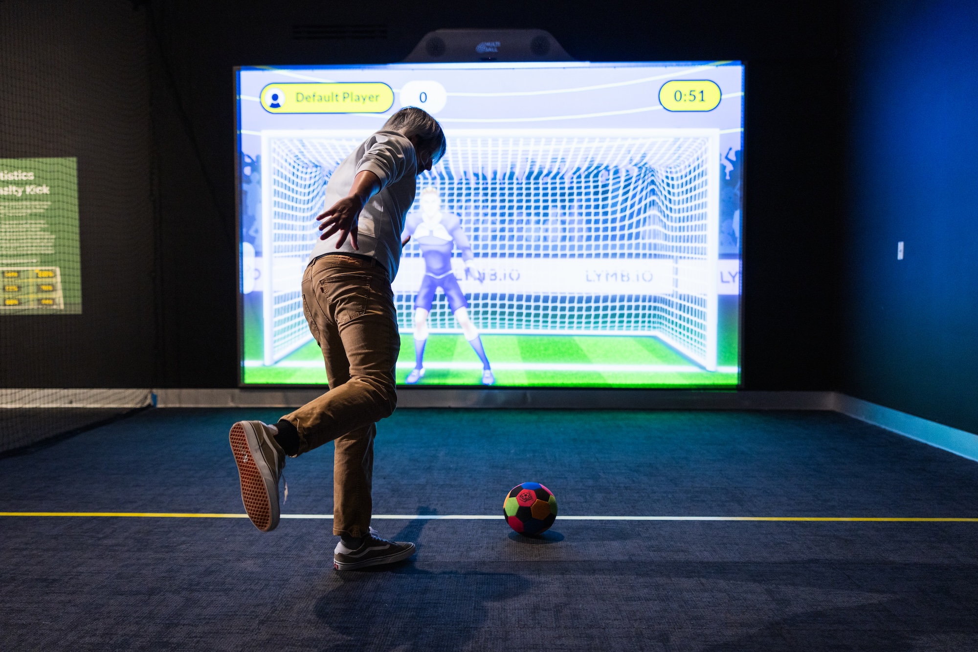 photo of a person kicking a soccer ball in front of an interactive screen showing an animated goalie in front of a soccer net