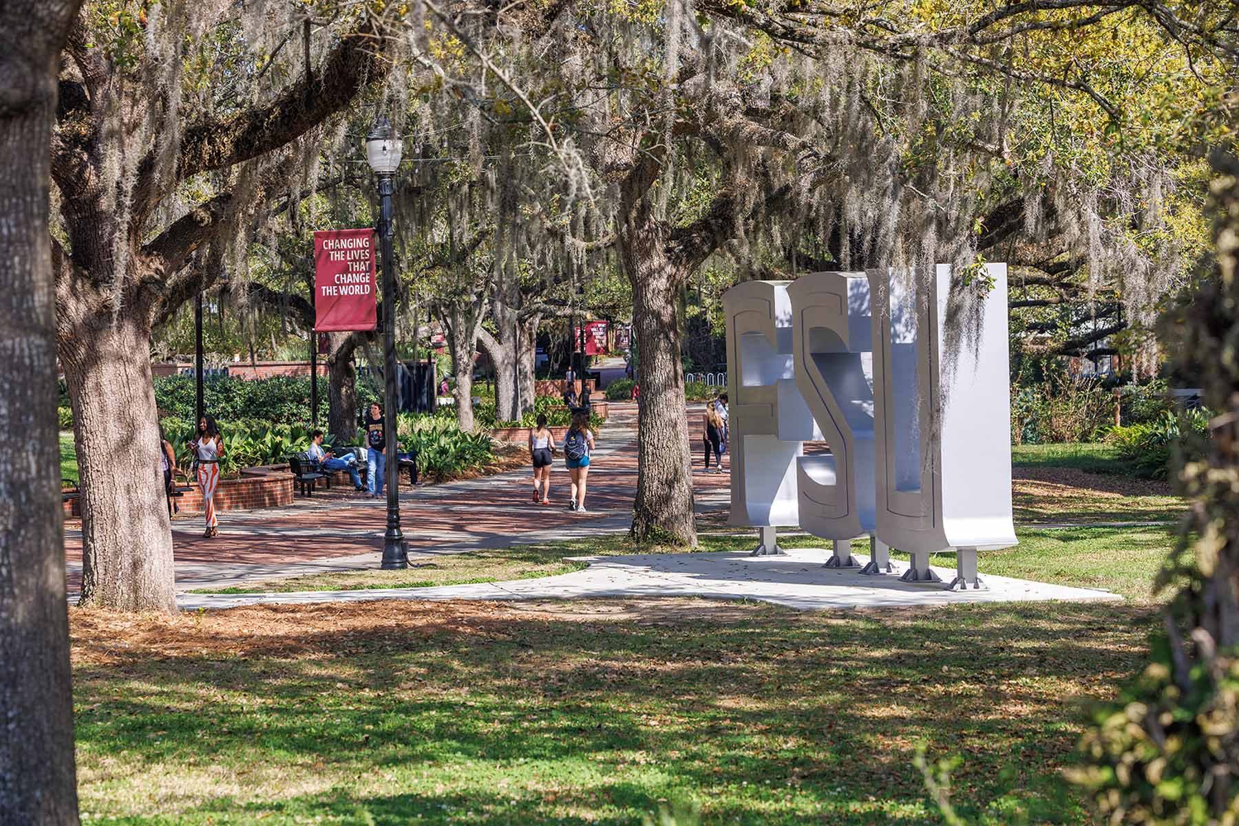 Students walk on Florida State University campus near the FSU sculpture beneath oak trees draped with Spanish moss.