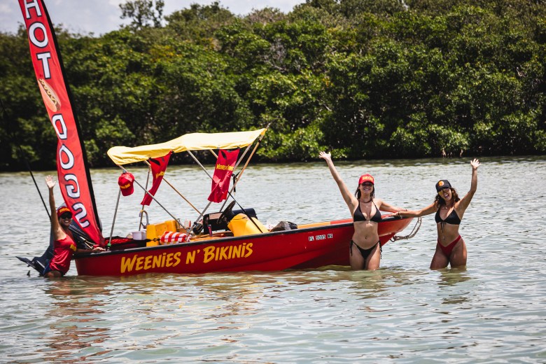The Weenies N' Bikinis hot dog boat with smiling, waving girls in bikinis on each side.