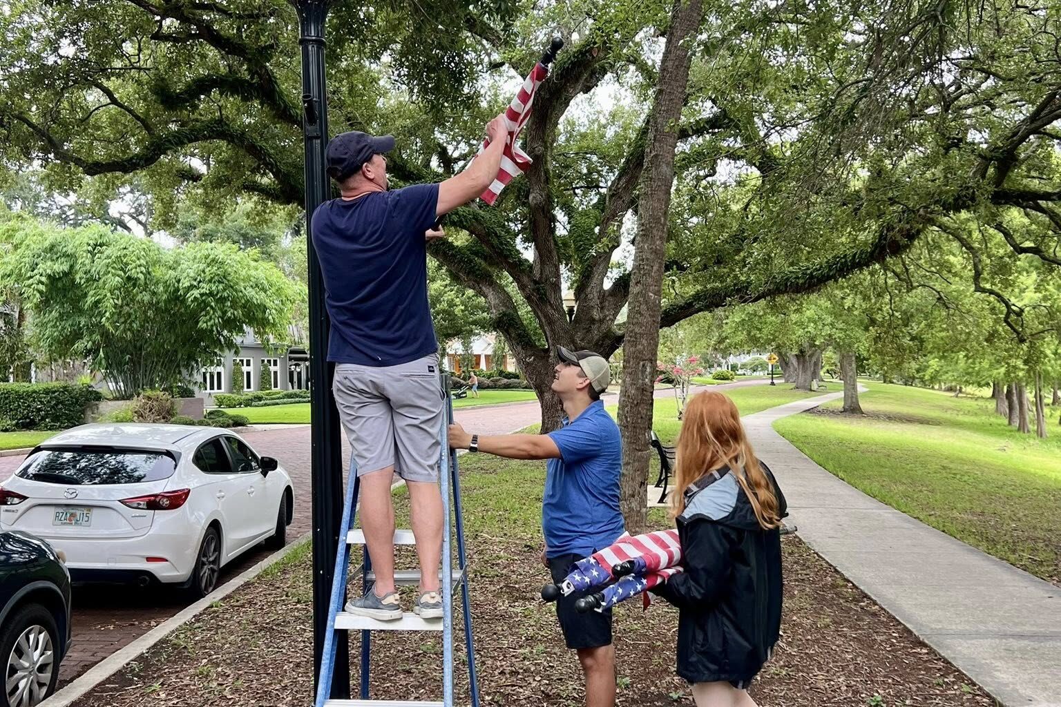People hanging flags around a lake, one on a ladder