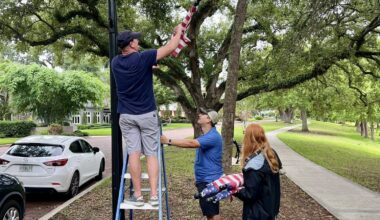 People hanging flags around a lake, one on a ladder