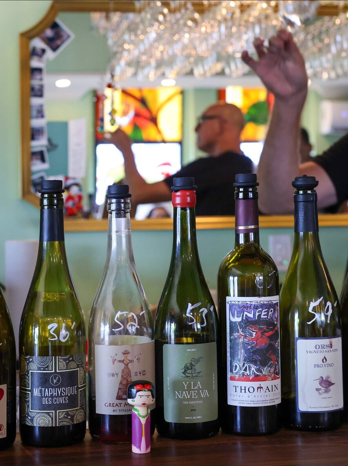Stephen Eisel checks and cleans a wine glass among wine bottles as patrons gather at the bar for a pour on Wednesday, June 10, 2026, in Hollywood, Florida. Champagne Shack is a small, independently owned wine bar located in Hollywood, Florida. Popular with local residents, it offers a relaxed atmosphere and regularly features food vendors on weekends, pop-up events with area restaurants, yoga sessions, a wine club, and live music or DJ performances in its intimate courtyard on Fridays and Saturdays.
