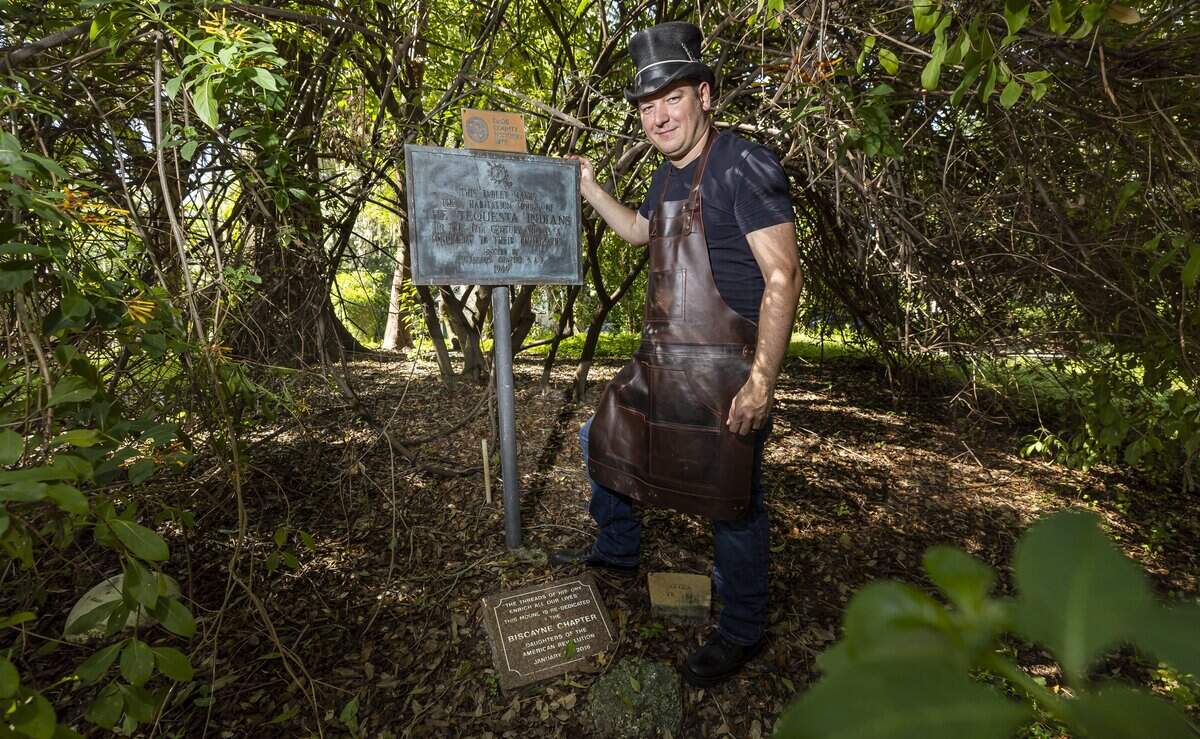 El Portal village council member Charles Winters, wearing the apron from his day job as a maker and restorer of stringed musical instruments, shows off a historic marker at the preserved prehistoric Tequesta Indian burial mound across the street from his home and workshop.