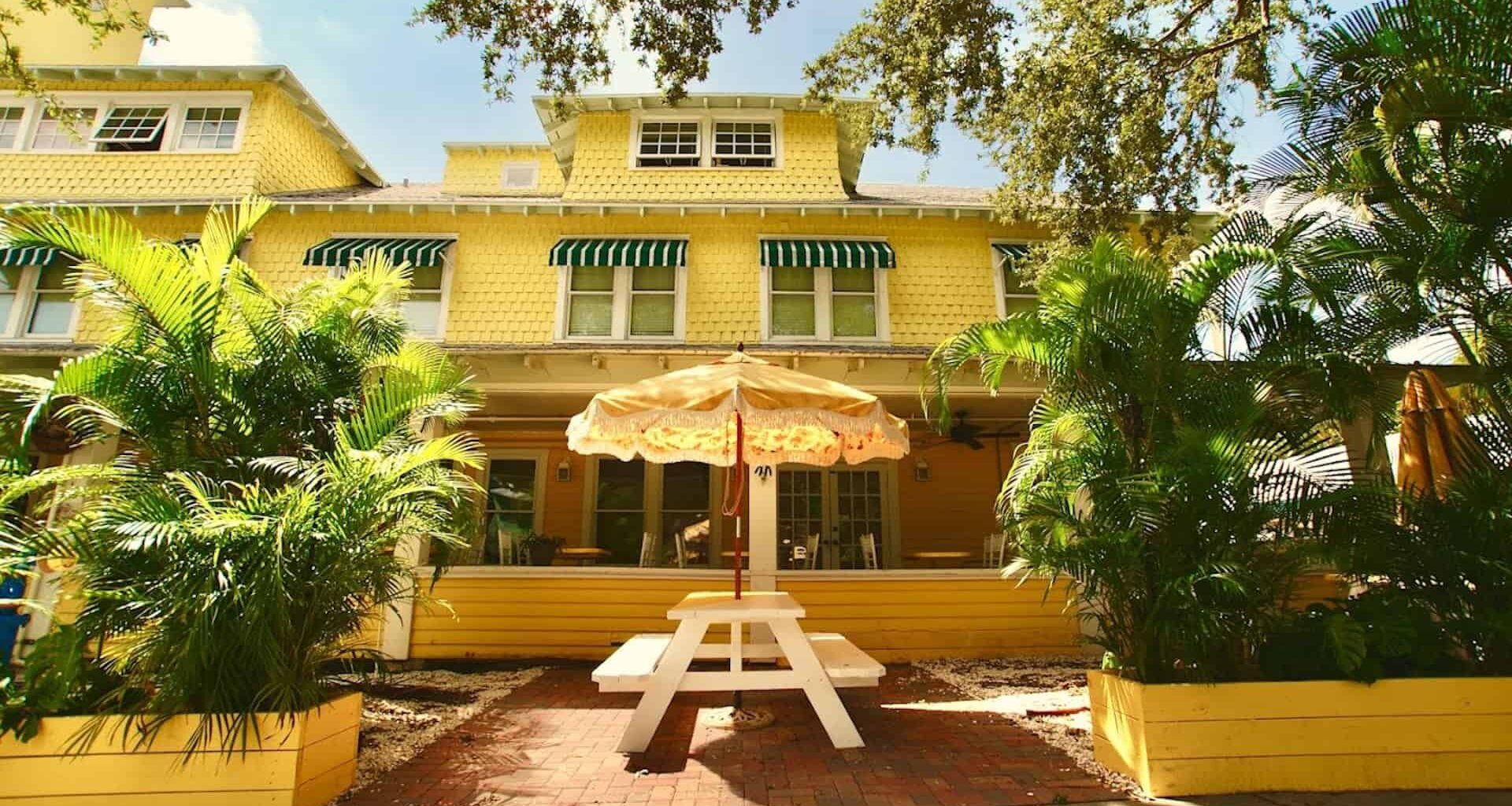 Exterior of a bed and breakfast with a yellow paint job and a picnic table with a yellow umbrella out front