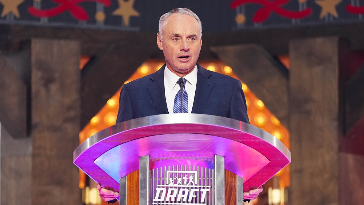 Commissioner Robert D. Manfred Jr. speaking at a podium at the 2024 MLB Draft event.