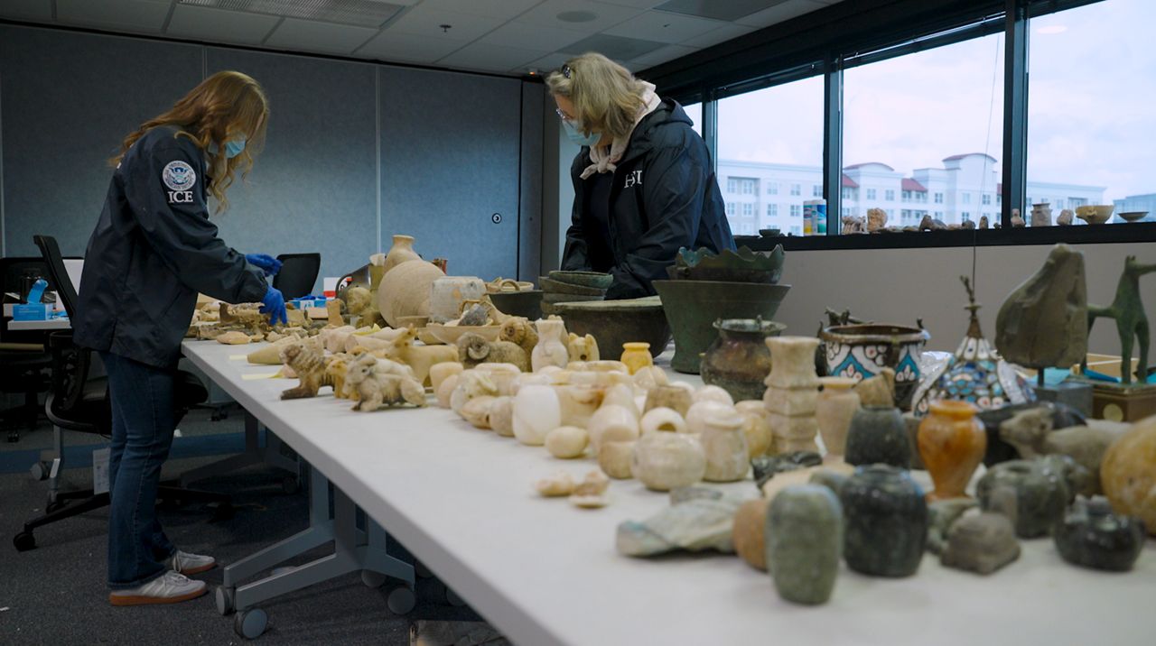 Two Homeland Security agents inspect thousands of artifacts, now evidence. (Spectrum News)