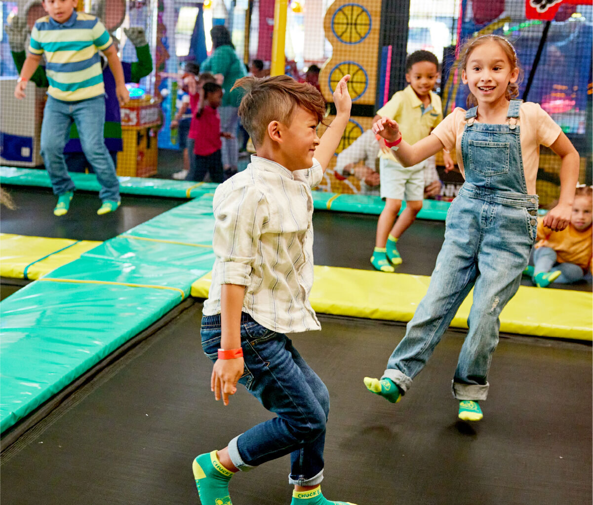 Kids jumping on trampolines at Chuck E. Cheese indoor playground with arcade games in the background