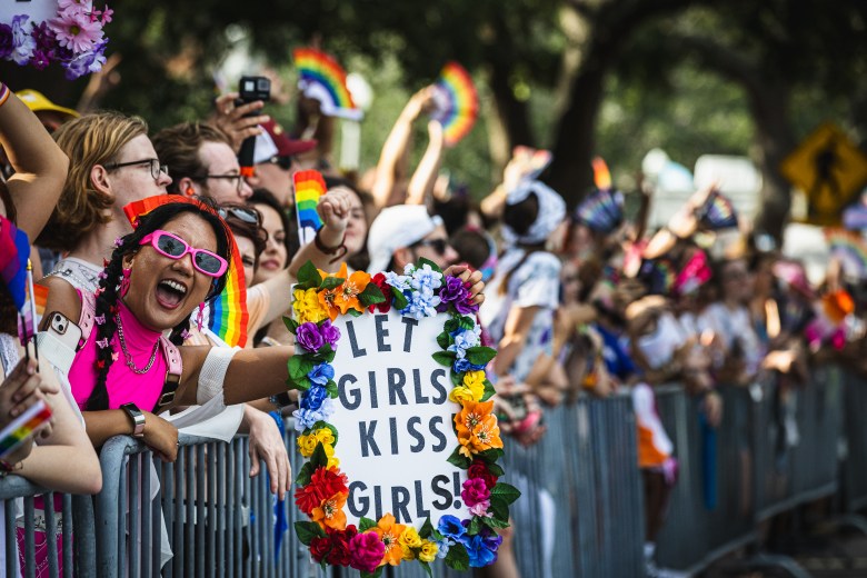 St. Pete Pride attendees including someone holding a sign reading 'let girls kiss girls.'