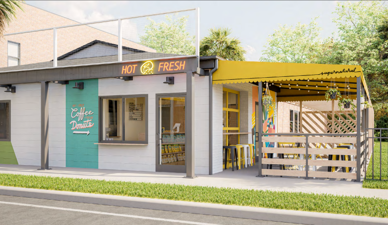 A digital architectural rendering of the upcoming Supernatural Food & Wine expansion in Tampa's West River neighborhood. The structure features a modern, clean design with a white-painted brick facade accented by a striking teal-colored rectangular panel on the left. A walk-up window for 'Coffee & Donuts' is visible. To the right, a bright, sunny yellow awning covers an outdoor patio area enclosed by a horizontal white-slat wooden fence, with string lights and hanging plants suggesting a cozy, welcoming atmosphere. The building is situated next to a sidewalk and mature trees under a clear, bright sky, conveying a polished and airy neighborhood aesthetic.