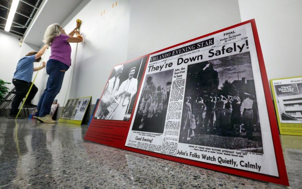 A copy of a March 23, 1965, front page proclaiming the safe return of the Gemini 3 crew is readied by Orange County Regional History Center exhibit associate Aidan McQuire and volunteer Eleanor Ackermann during the installation of a new pocket exhibit commemorating the Orlando Sentinel's 150th anniversary, Thursday, June 4, 2026. The exhibit opening June 6 is titled "Extra! Extra! The Orlando Sentinel Turns 150" and showcases photographs, archival materials, and artifacts from the Sentinel's origin as the Orange County Reporter in 1876 to Florida's second-largest newspaper in the 21st century. (Joe Burbank/Orlando Sentinel)