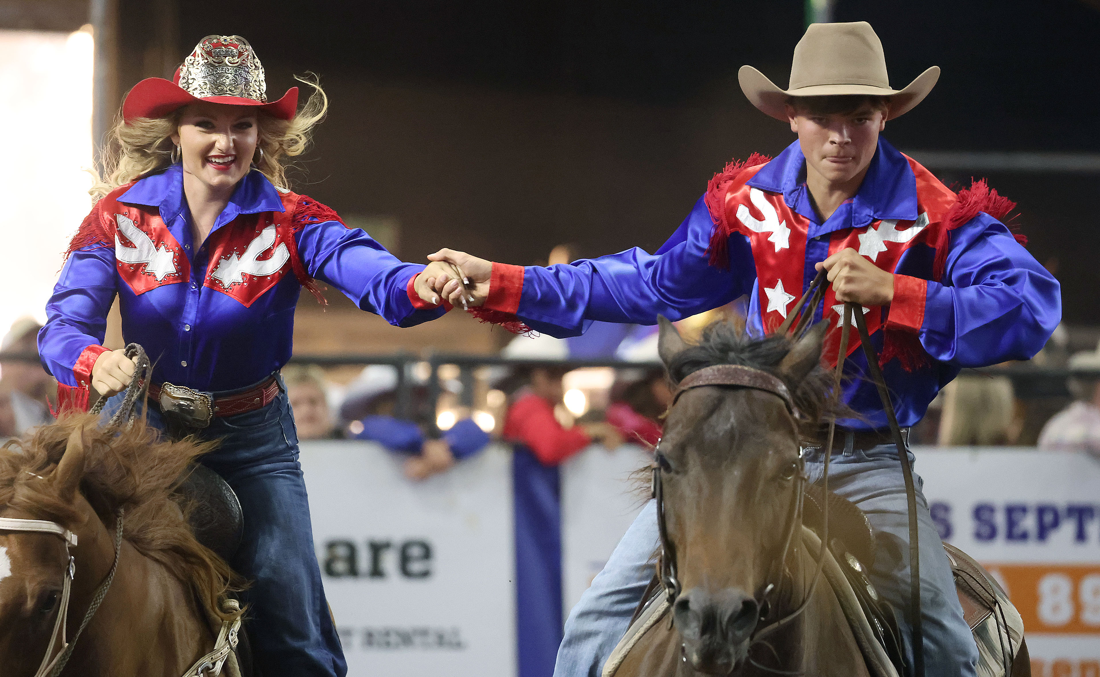 A cowboy and cowgirl hold hands while riding during the...