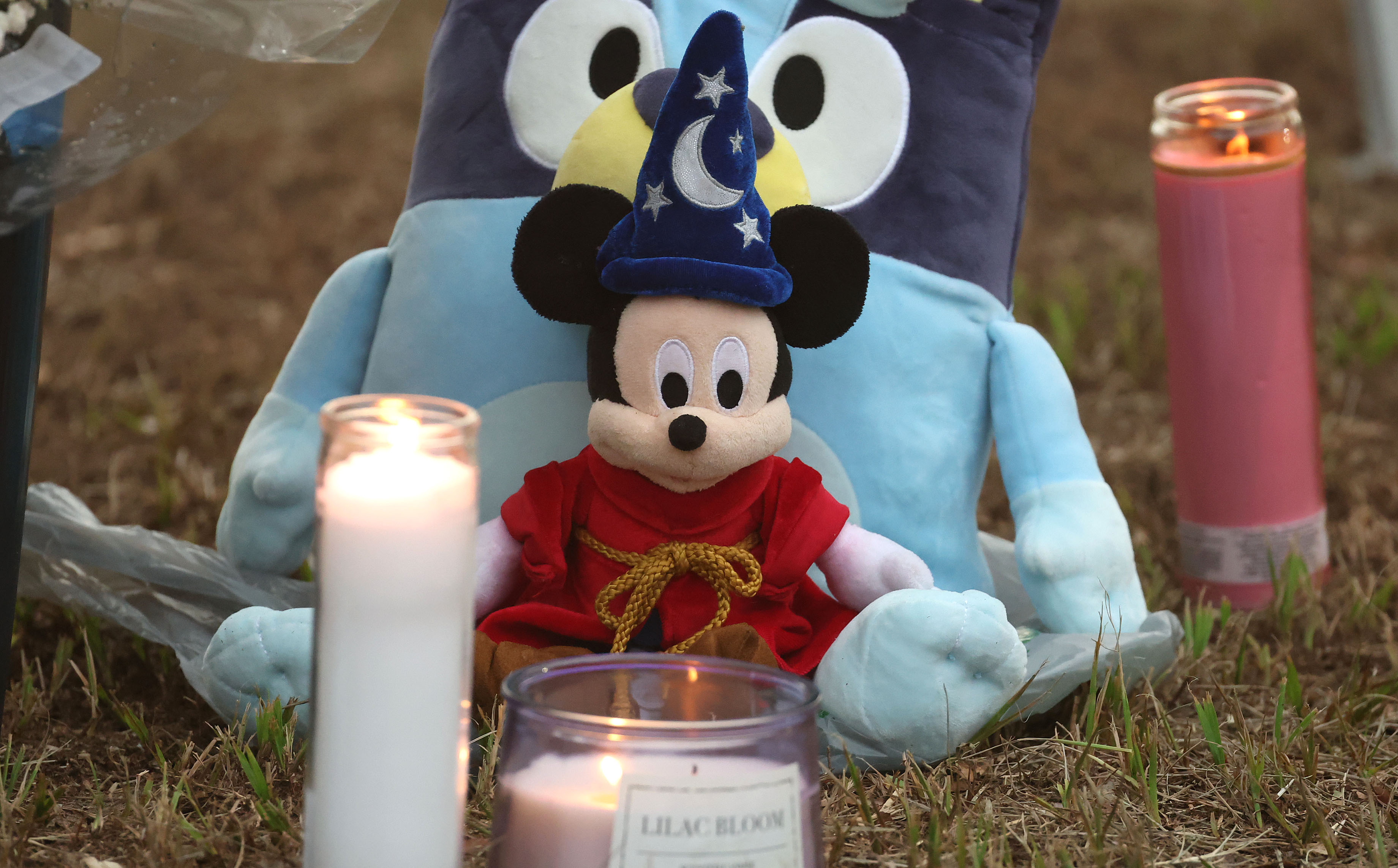Stuffed animals and lighted candles rest in the lawn during...
