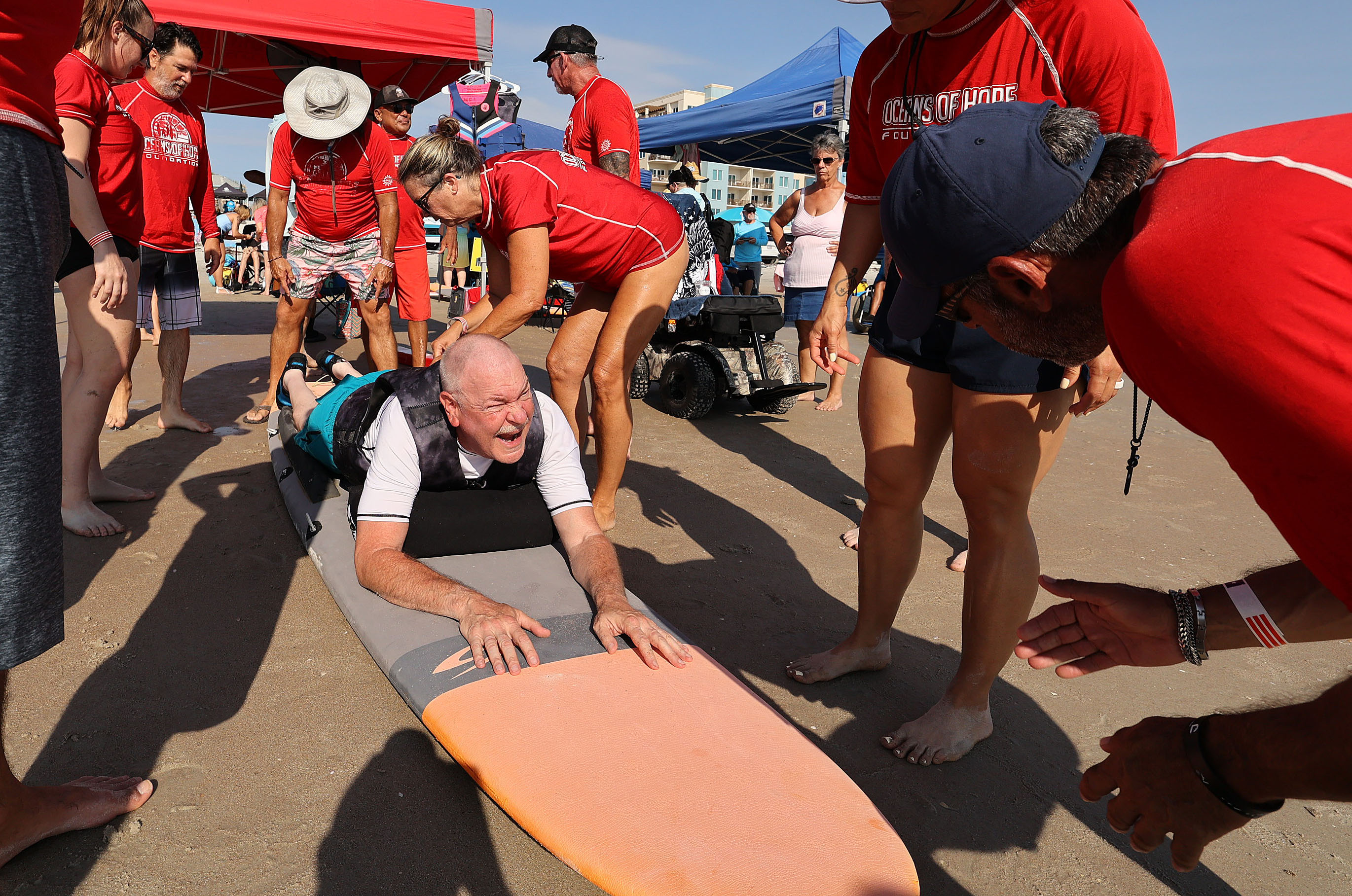 Volunteers help Navy veteran Rick Rettinger (bottom) onto a surfboard...