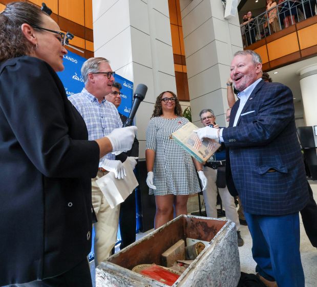 RETRO REVEAL Orlando mayor Buddy Dyer notices the 305 area code for an Orlando phone book from 1976 during the opening of a 50-year-old time vault at city hall ahead of America's 250th celebration Monday, June 29, 2026. The vault was sealed and buried at Lake Eola by the Kiwanis during the nation's Bicentennial celebration in 1976. From left, City of Orlando's Tara Russakov; Matt Kelly, Orlando Kiwanis Club; commissioners Tony Ortiz and Shan Rose. The vault revealed a preserved collection of newspapers, photographs and Central Florida memorabilia.(Joe Burbank/Orlando Sentinel)