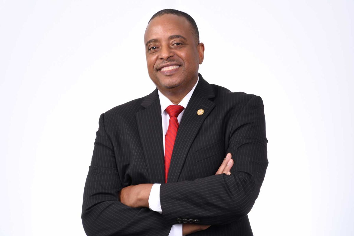 Headshot of Ted Ellis in a black suit with red tie against a white background.