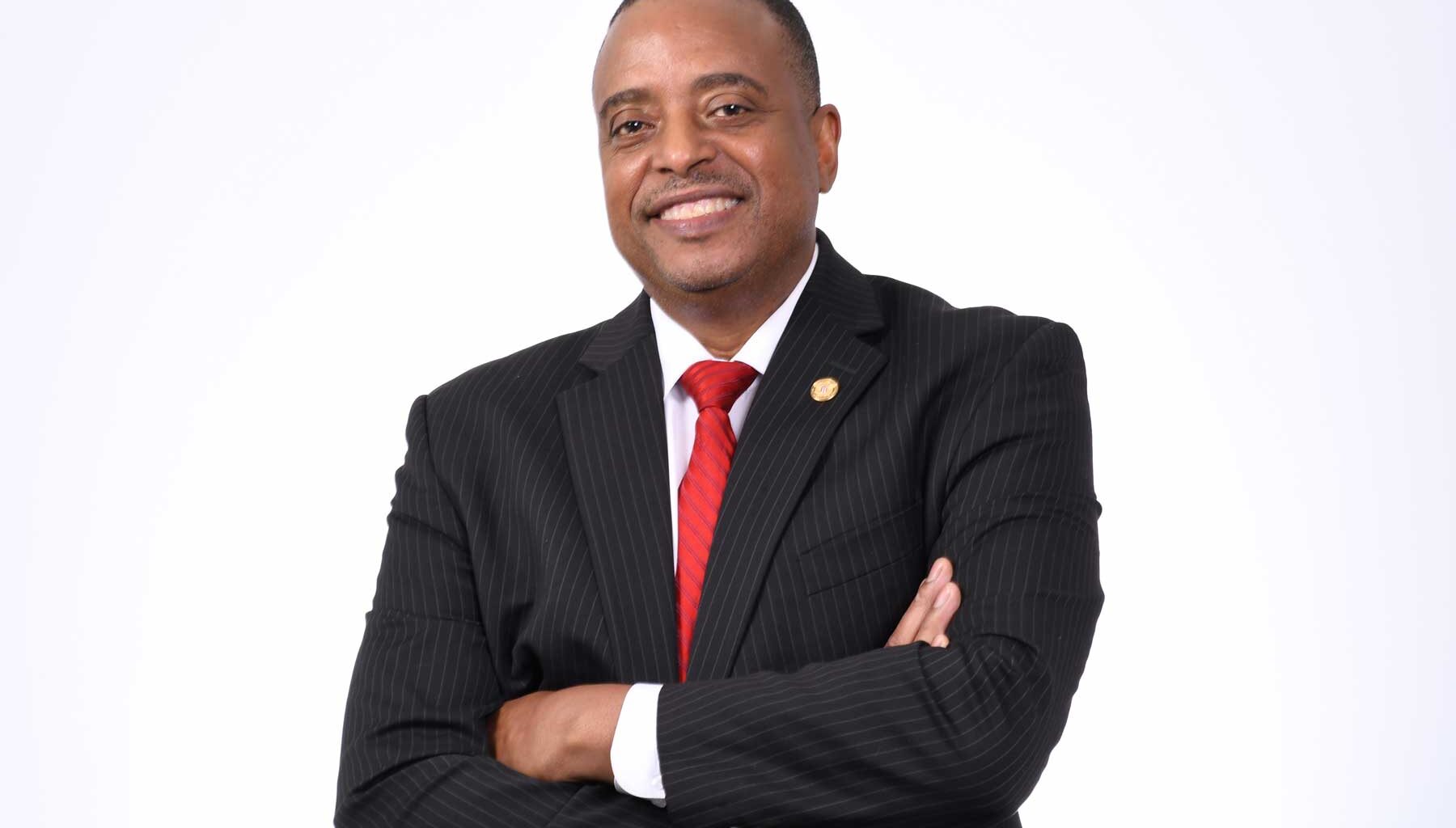 Headshot of Ted Ellis in a black suit with red tie against a white background.