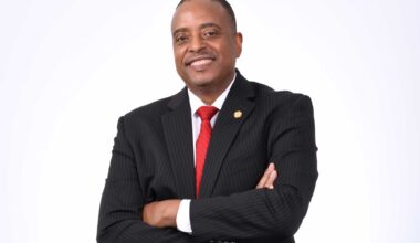 Headshot of Ted Ellis in a black suit with red tie against a white background.