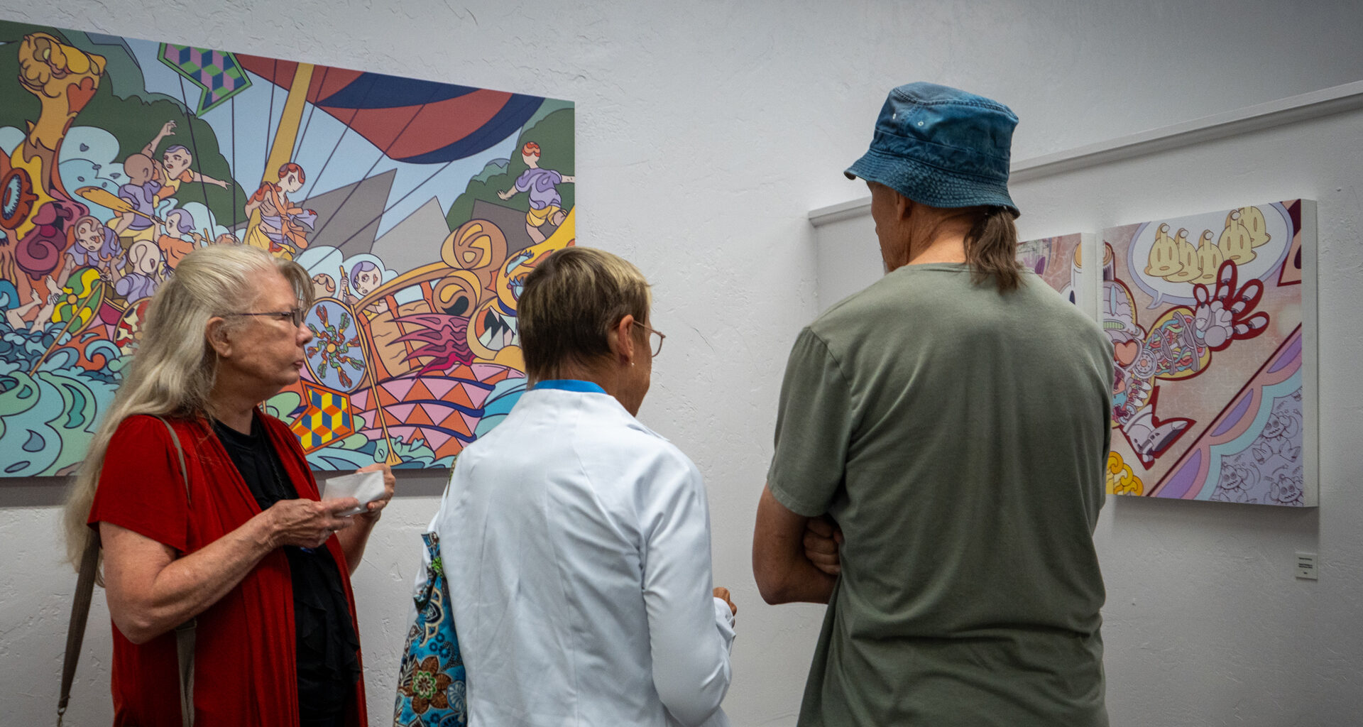A photograph of three people viewing colorful, abstract paintings in an art gallery with white walls.