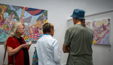 A photograph of three people viewing colorful, abstract paintings in an art gallery with white walls.