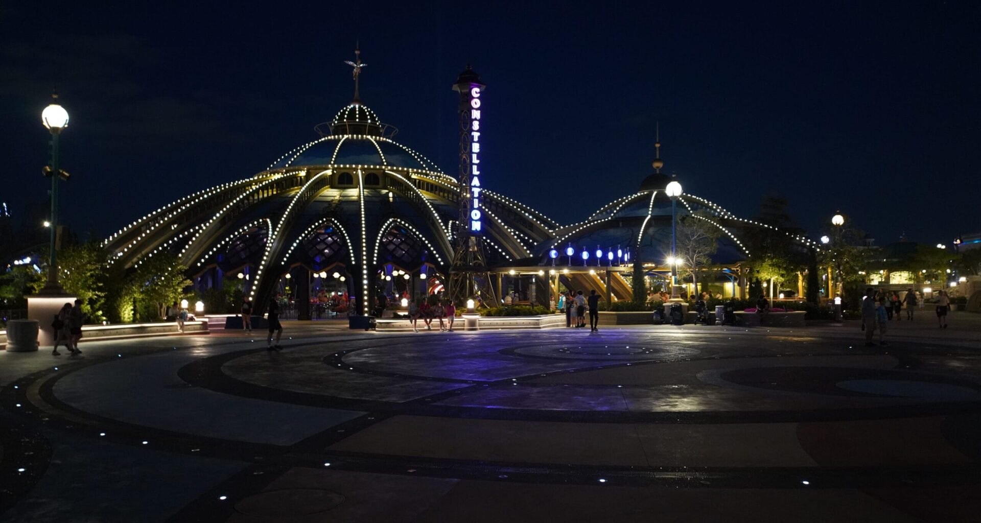 A dome-shaped pavilion with glowing lights at night, as people stroll the Universal Epic Universe plaza on the 4th of July.