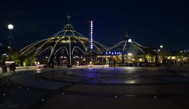 A dome-shaped pavilion with glowing lights at night, as people stroll the Universal Epic Universe plaza on the 4th of July.