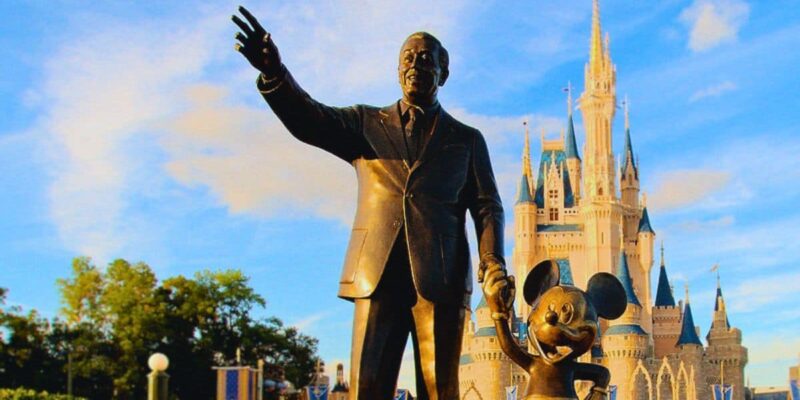 Walt Disney and Mickey Mouse statue in front of Cinderella Castle at Disney, with a bright blue sky and fluffy clouds above during the hot, humid summer months in Central Florida in Orlando. Florida resident Disney Summer Ticket