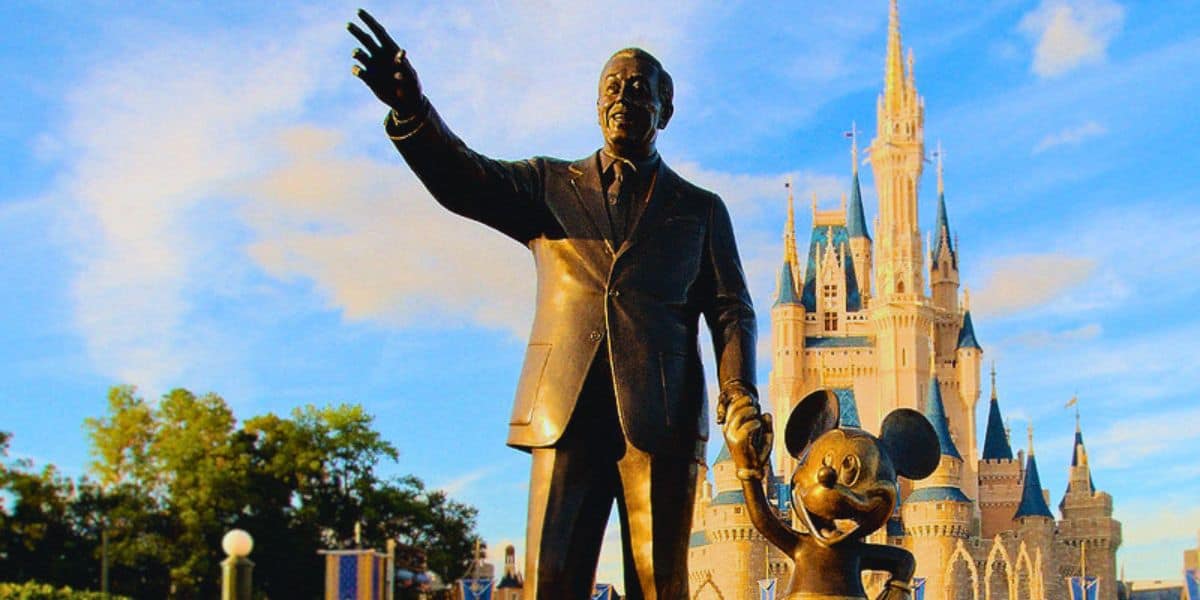 Walt Disney and Mickey Mouse statue in front of Cinderella Castle at Disney, with a bright blue sky and fluffy clouds above during the hot, humid summer months in Central Florida in Orlando. Florida resident Disney Summer Ticket