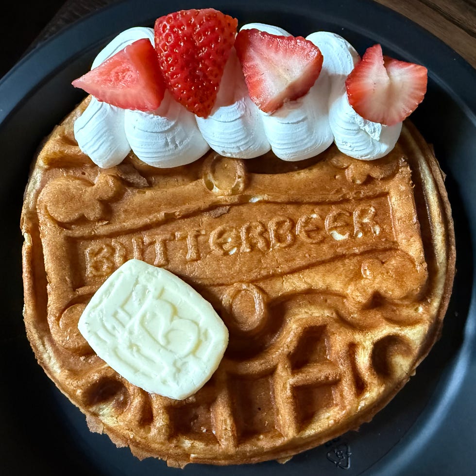 Round waffle with butter, whipped cream, and strawberries on a black plate. Round waffle with butter, whipped cream, and strawberries on a black plate.