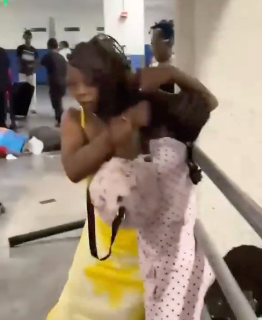 Two women fighting, one in a yellow dress and one in a polka dot outfit, in a public area.