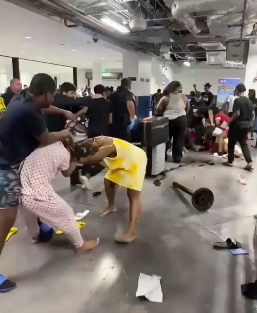 A group of people fighting in a crowded hall, with some individuals on the floor and others attempting to intervene.