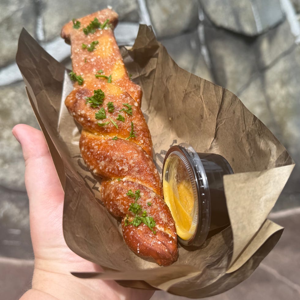 Hand holding a twisted pretzel garnished with herbs, served with dipping sauce. Hand holding a twisted pretzel garnished with herbs, served with dipping sauce.